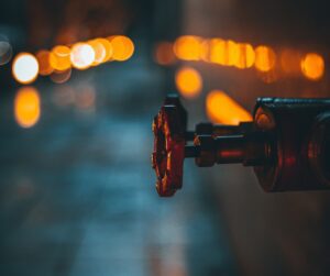 Close-up of a plumbing valve with blurred orange lights in the background, symbolizing Frost & Kretsch Plumbing's expertise in reliable plumbing services in Richmond.