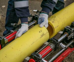 Worker connecting yellow plumbing pipe using specialized equipment, highlighting plumbing services related to installation and repairs in Richmond.