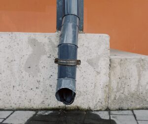 Drain pipe discharging water onto concrete surface, illustrating plumbing infrastructure relevant to Frost & Kretsch Plumbing's repair services in Ray, Michigan.